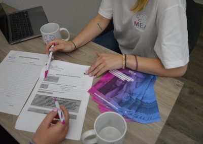 Zwei Personen am Tisch beim Ausfüllen von MEA-Dokumenten: Auf dem Tisch liegen ein Arbeitszeitnachweis, eine Vollmacht, mehrere MEA-Flyer, ein Laptop und zwei Tassen mit dem MEA-Logo.